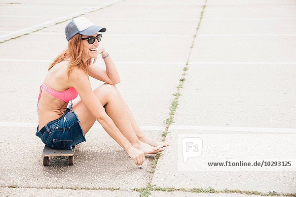 Mittlere erwachsene Frau auf dem Skateboard sitzend. Lachend.
