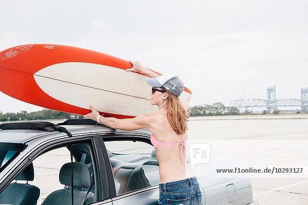 Mittlere erwachsene Frau am Strand,  Entfernen des Surfbrettes vom Autodach
