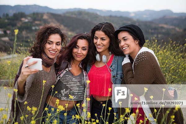 Four adult sisters posing for smartphone selfie on rural road