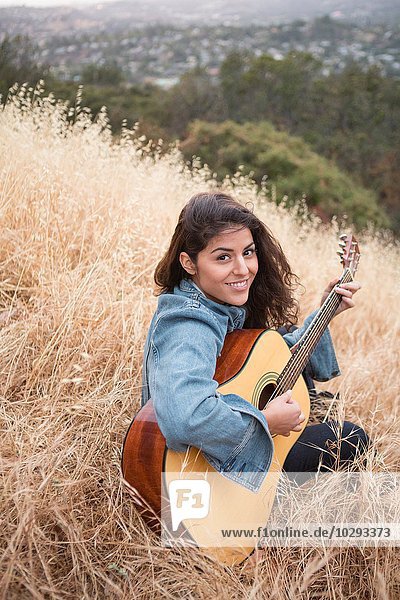 Portrait of young woman playing acoustic guitar on grassy hill