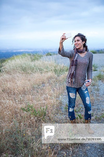 Junge Frau posiert für Smartphone Selfie auf ländlichem Hügel