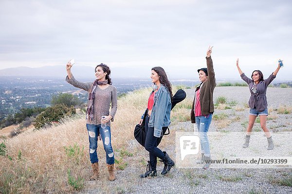 Four adult sisters posing for smartphone selfie on rural hill