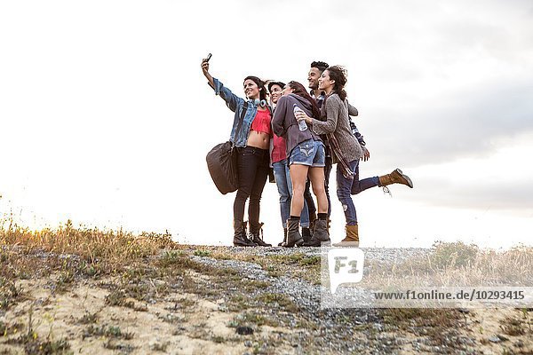Young man and four adult sisters posing for smartphone selfie on dirt track