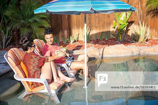 Young man and sister chatting on garden lounge chairs