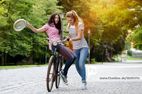 Junge Frau mit Hut auf dem Sattel auf dem Fahrrad mit Freund beim Schieben