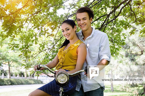 Junges Paar im Park mit Fahrrad und lächelndem Blick auf die Kamera