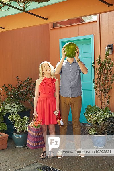 Frau mit Weinflasche und Mann  der das Gesicht mit Wassermelone bedeckt.
