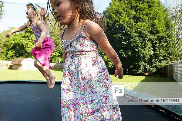 Zwei Mädchen springen auf Trampolin im Garten