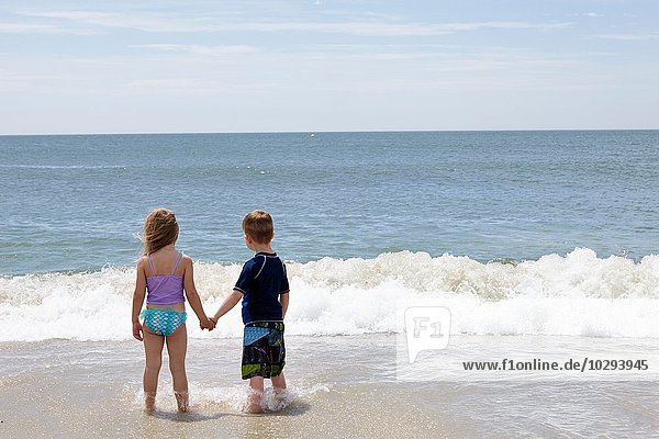 Rear view of girl and boy holding hands in sea