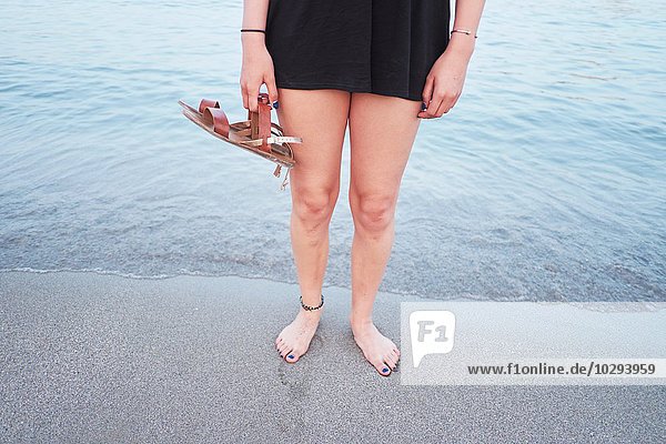 Taille unten von junger Frau am Strand mit Sandalen