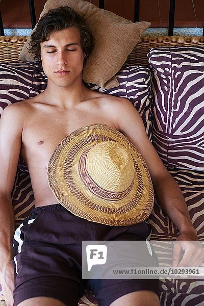 Junger Mann liegt auf einer Liege mit Sonnenhut im Bauch
