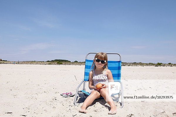 Porträt eines Mädchens mit Sonnenbrille auf einem Liegestuhl am Strand