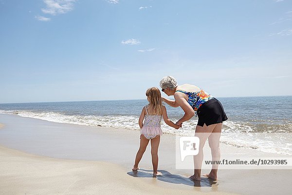Seniorin zeigt auf Enkelin am Strand