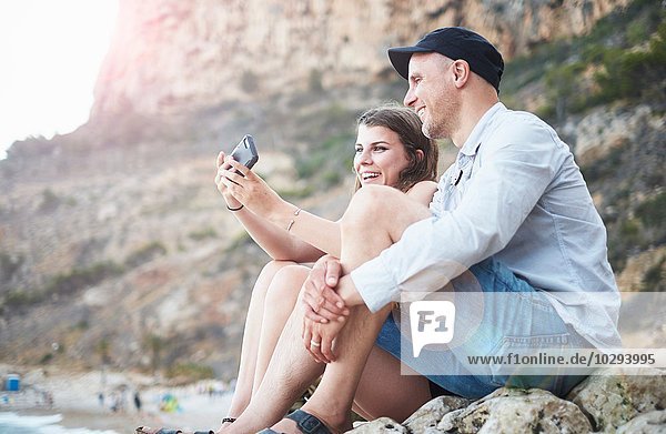 Erwachsener Mann und Teenager-Tochter beim Lesen von Smartphone-Texten am felsigen Strand  Javea  Spanien