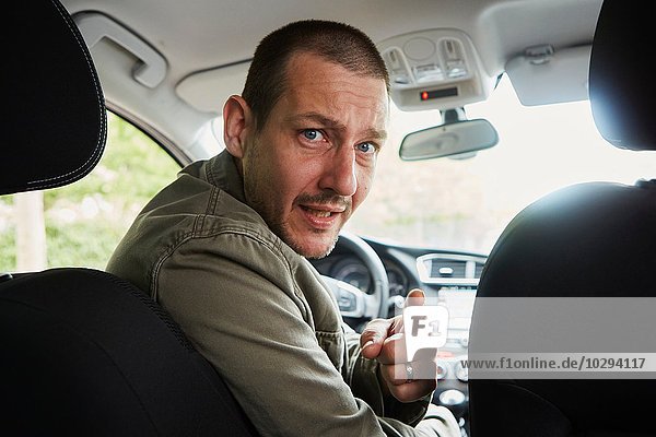 Mid adult man sitting in car  leaning over to back seat  pointing
