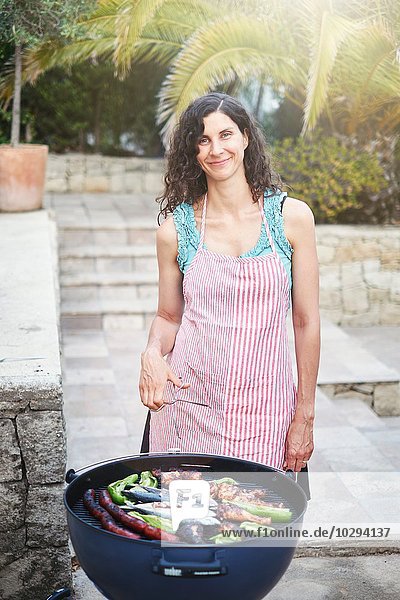 Porträt einer reifen Frau bei der Zubereitung von Grillgerichten auf der Terrasse