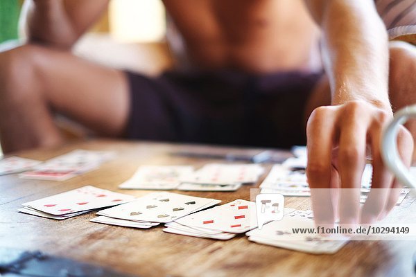 Ausschnitt eines jungen Mannes  der am Tisch Karten spielt.