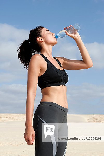 Mittlere erwachsene Frau  die aus der Wasserflasche trinkt  während sie am Strand trainiert.