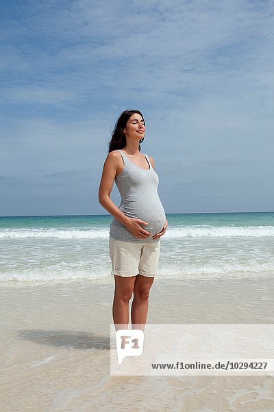 Schwangere mittlere erwachsene Frau stehend mit geschlossenen Augen im Meer