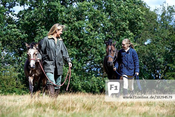 Mother and daughter walking horses in field