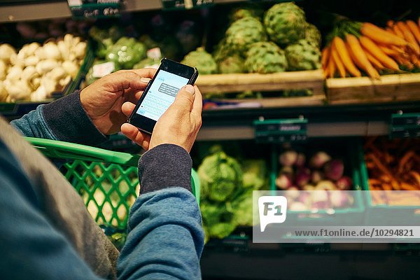 Mann einkaufen und Smartphone im Supermarkt benutzen