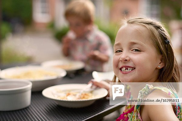 Mädchen beim Essen am Gartentisch  Blick über die Schulter lächelnd in die Kamera