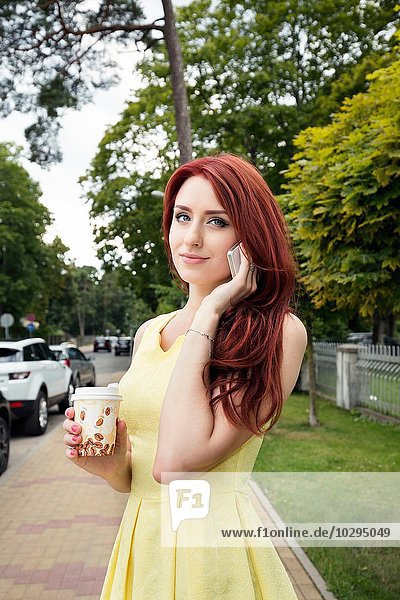 Young woman with coffee cup using smartphone on street