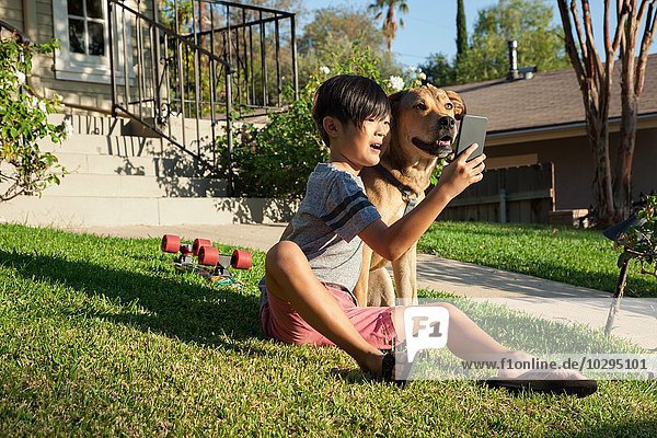 Boy posing for smartphone selfie with dog in garden