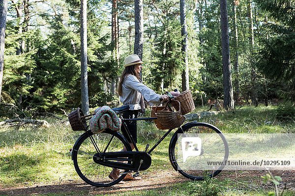 Mature woman cyclist with foraging baskets on forest path