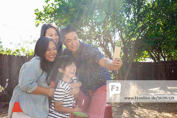 Familie mit Junge posiert für Smartphone Selfie im sonnigen Garten