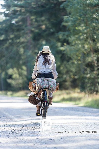 Rear view of woman cycling on forest road with foraging baskets