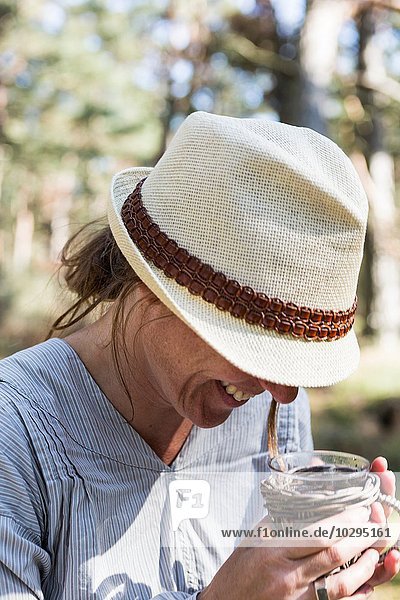 Mature woman laughing whilst drinking tea in forest