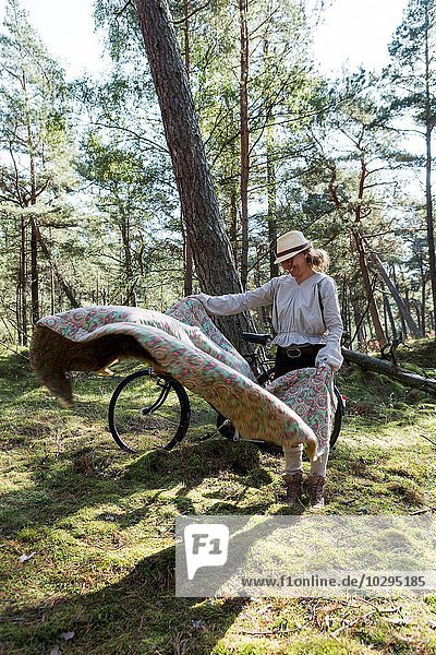 Mature female cyclist laying down blanket on forest floor
