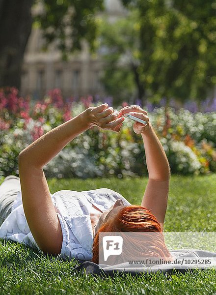Mittlere erwachsene rothaarige Frau auf Gras liegend mit Smartphone