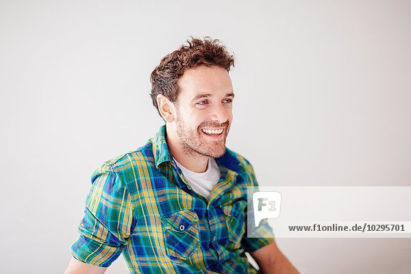 Porträt eines erwachsenen Mannes mit kariertem Hemd  der lächelnd wegschaut.