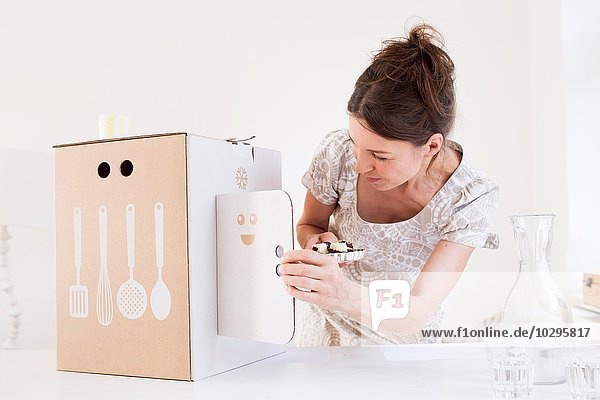 Reife Frau hält Backwaren mit Blick auf Karton mit Küchenutensilien-Motiv