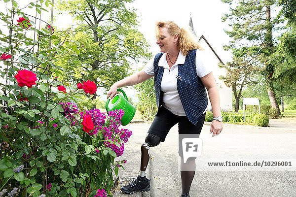 Mittlere erwachsene Frau mit Beinprothese  im Garten  Pflanzen gießen