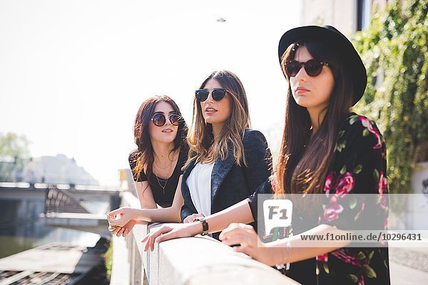 Drei stilvolle junge Freundinnen  die vom Flussufer der Stadt aus schauen