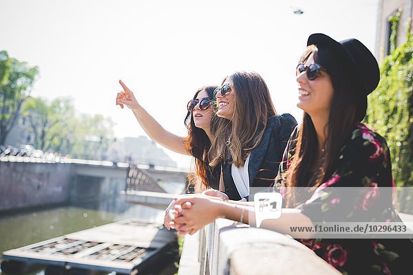 Drei stilvolle junge Freundinnen  die vom Flussufer der Stadt aufblicken.