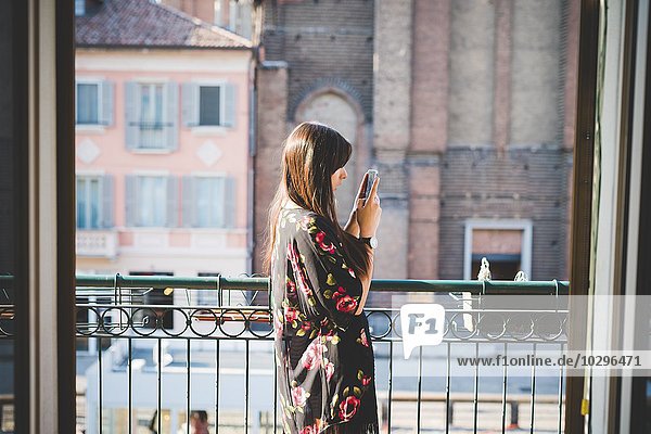 Junge Frau liest Smartphone-Texte auf dem Stadtbalkon