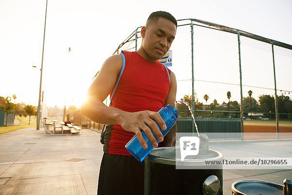 Junger Mann füllt Wasserflasche aus Getränkebrunnen