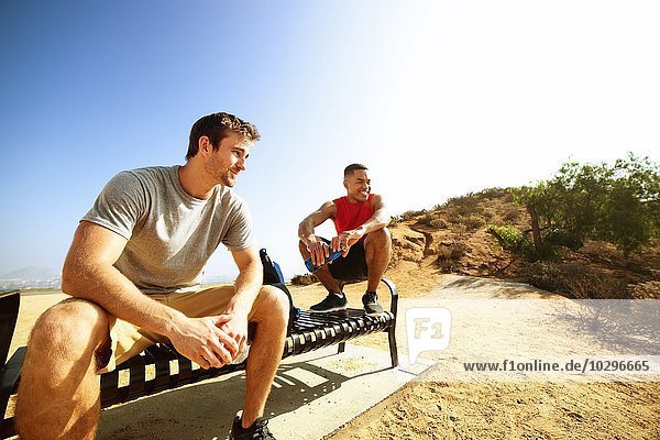 Two male friends  sitting on bench  on cliff top  looking at view