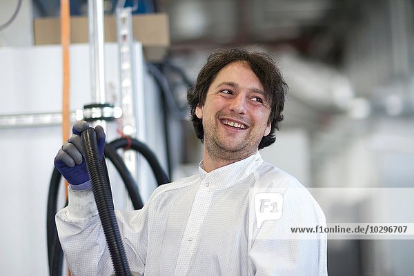 Mittlerer erwachsener Mann im Laborkittel mit Industrie-Rohrleitung  lächelnd wegblickend