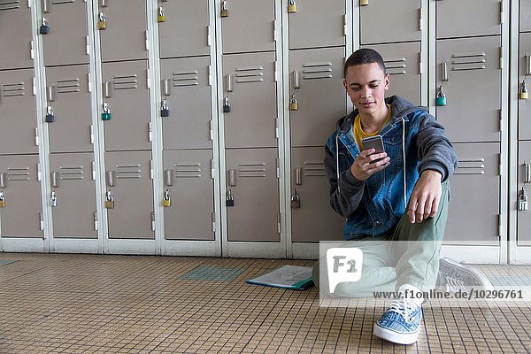 Student lehnt sich an Schließfächer  mit Smartphone