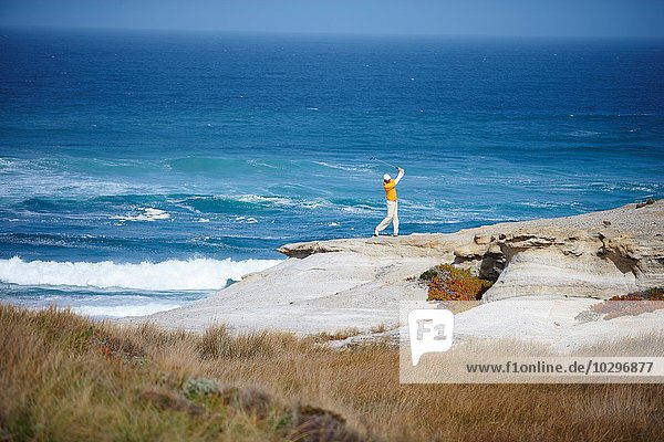 Hochwinkelansicht des Golfspielers  der auf einer Klippe mit Blick auf den Ozean steht und einen Golfschwung macht.
