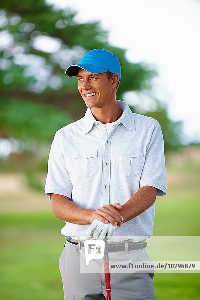 Golfer wearing golf glove and baseball cap holding golf club looking away smiling