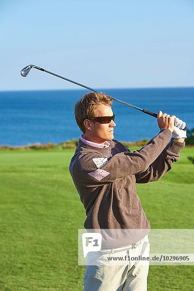 Golfer mit Sonnenbrille nimmt Golfschwung und schaut weg.