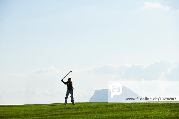 Golfer beim Golfschwung vor der Bergkette