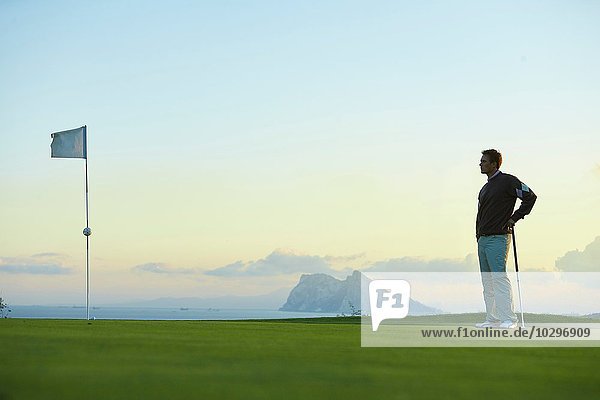 Golfer  der den Golfschläger in der Nähe der Golfflagge hält  schaut weg.