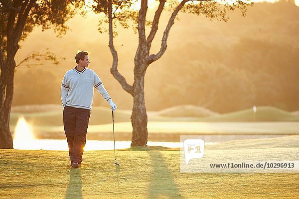 Golfer im Sonnenlicht  der sich gegen den Golfschläger lehnt  Hand in Hand mit Blick in die Tasche